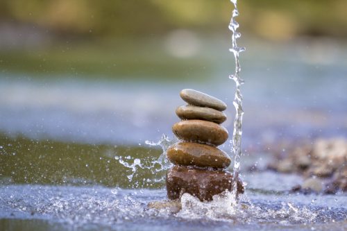 Close-up abstract image of water pouring down on rough natural brown uneven different sizes and forms stones balanced like pyramid pile landmark on blurred blue-green misty copy space background.
